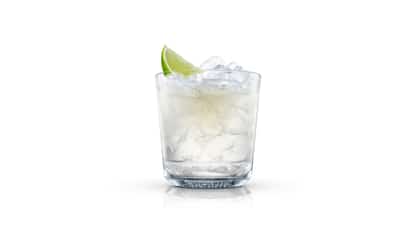 A clear mixed cocktail over crushed ice in an Absolut rocks glass with a lime wedge on white background.