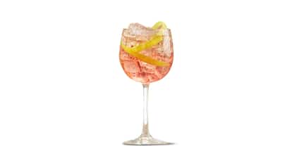 Strawberry Punch in a wine glass with ice and a lemon peel on white background
