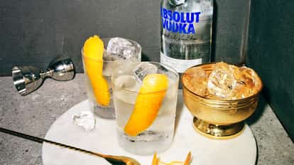 Summertime Cookout in two rocks glasses with ice and orange peels and Absolut Vodka bottle in background on marble