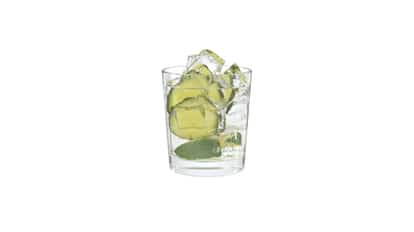 The Alchemist in a rocks glass with ice cubes and lime wedge on white background