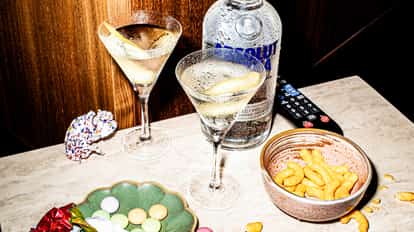 Two Vesper Martini cocktails next to a bottle of Absolut and two bowls of snacks.