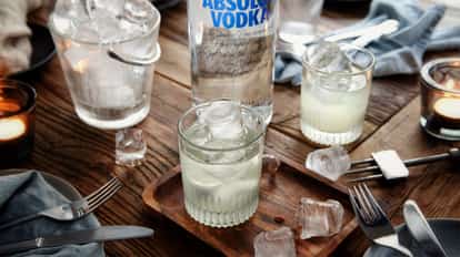 Iceberg cocktail in a ribbed rocks glass with ice beside an Absolut Vodka bottle on a wooden table
