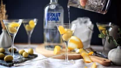 Vodkatini in a martini glass with olives and a lemon twist and an Absolut vodka bottle in the background