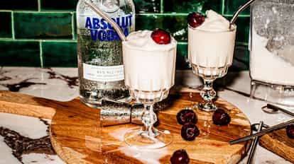 Volcano in stemmed glasses with frozen foam and cherries and an Absolut Vodka bottle behind