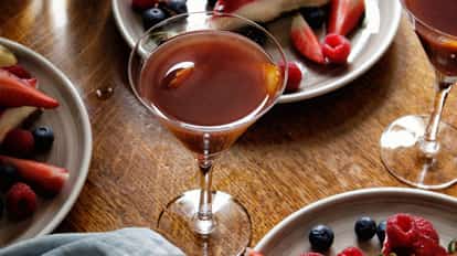 Volga Boatman in a stemmed cocktail glass with an orange peel, on a wooden table with plates of berries.