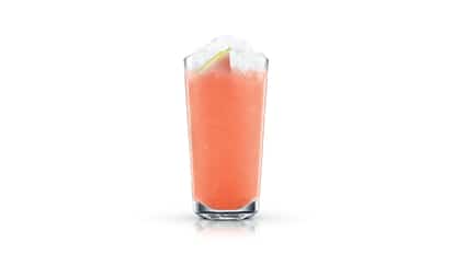 Watermelon Lemonade in a tall highball glass topped with crushed ice and a lime wedge on white background.