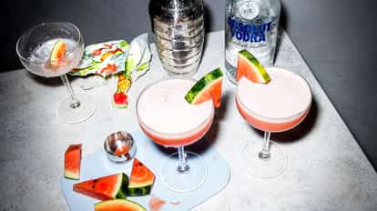 Two Watermelon Martini cocktails beside a bottle of Absolut Vodka on a glass table.