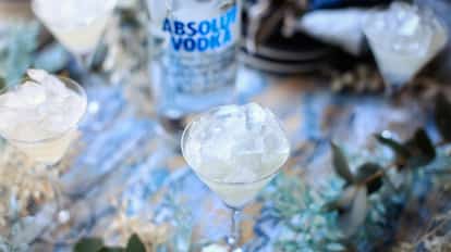 X-rated cocktail in a stemmed coupe topped with crushed ice and an Absolut vodka bottle in the background.